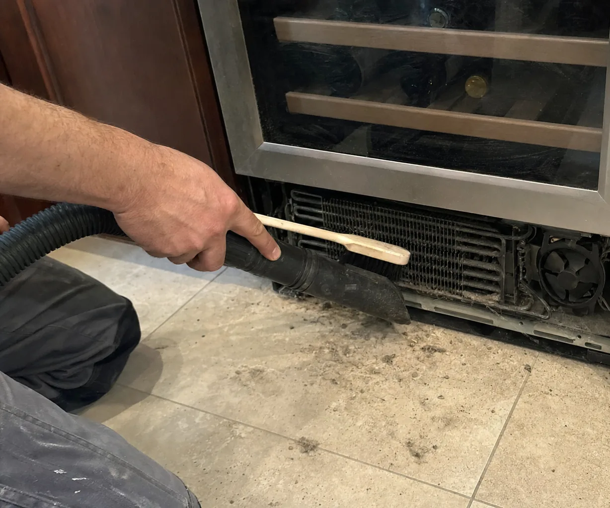 Left-hand crop of the open base of a refrigeration cabinet with the grille off and moisture marks on the tile